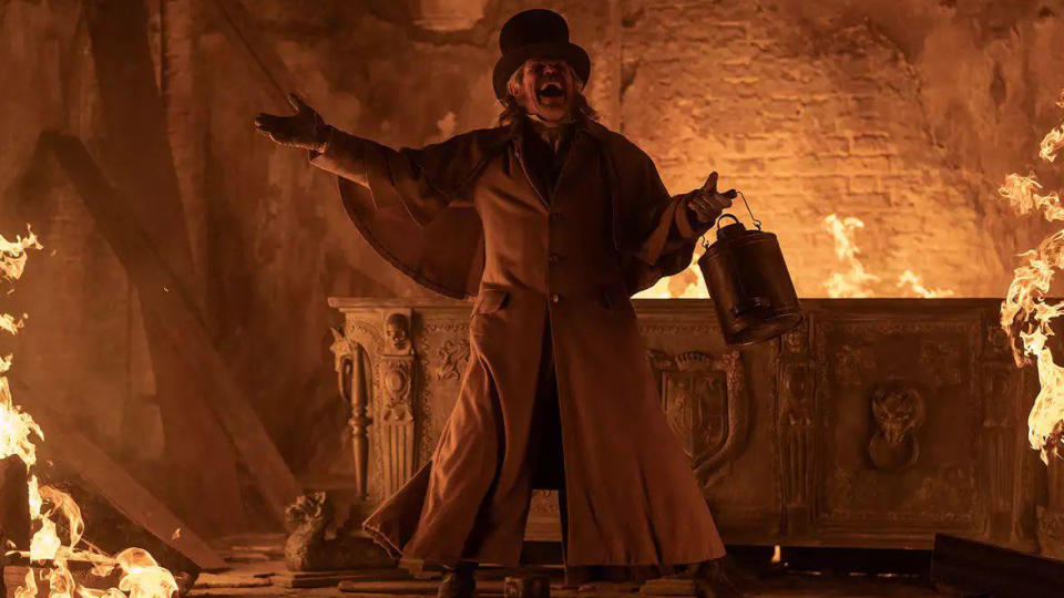 Willem DaFoe in Nosferatu, holding a lantern and laughing maniacally while a fire rages around him