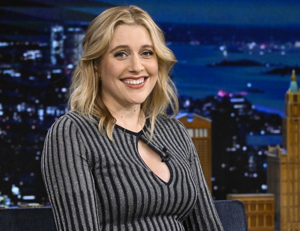 Greta Gerwig smiles at the audience while seated at a talk show desk