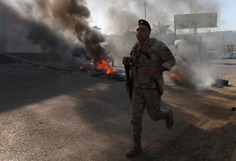 A Lebanese army soldier runs near burning tires during ongoing anti-government protests in Tripoli