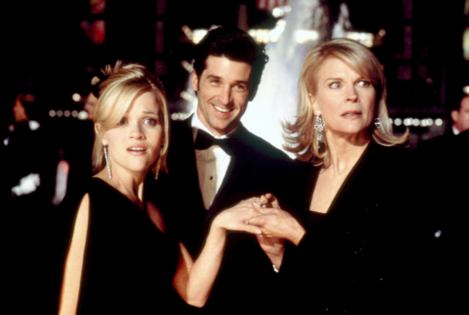 Candice Bergen holding Reece Witherspoon's hand with shocked expressions as Patrick Dempsey smiles widely between the two in a scene from "Sweet Home Alabmam"