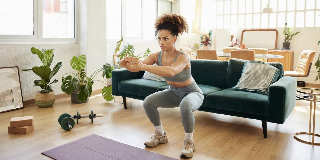 young fit woman doing squats in living room