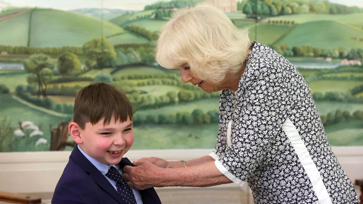 Queen Camilla adjusting the tie of a young boy in a wheelchair