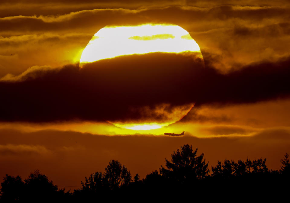 The sun rises over a forest as a plane passes by in Frankfurt, Germany, Wednesday, Oct. 6, 2021. (AP Photo/Michael Probst)