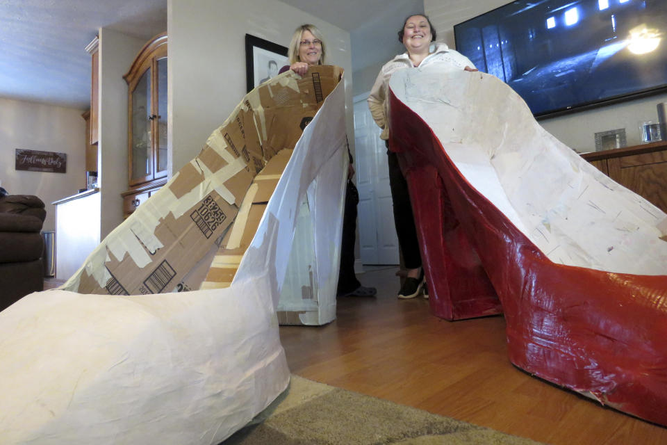 Charlotte "Charlie" Jallans-Daly, right, and her wife, Sharon Jallans-Daly, pose for a picture behind giant ruby slippers which are part of Wizard of Oz "house float" decorations for Mardi Gras. Wednesday, Jan. 13, 2021 in New Orleans. All around the city, thousands of houses are being decorated as floats because the coronavirus pandemic has canceled parades that usually take place on Mardi Gras. (AP Photo/Janet McConnaughey)