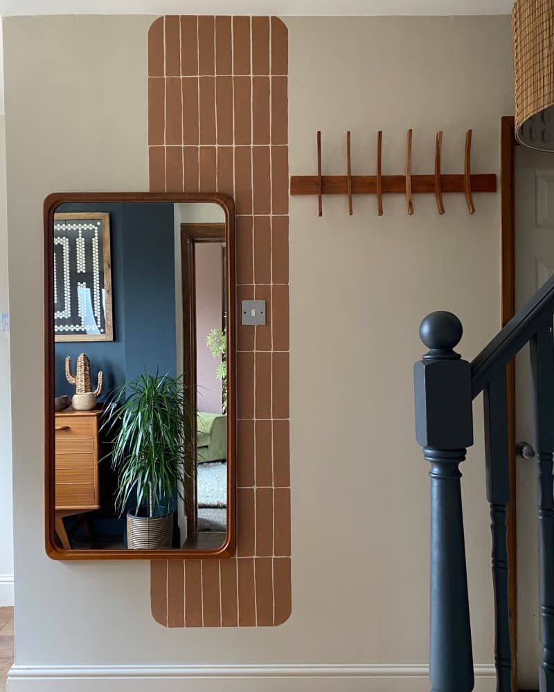 Mirror, decorative paint element, and wood hooks on neutral wall next to dark painted railing.