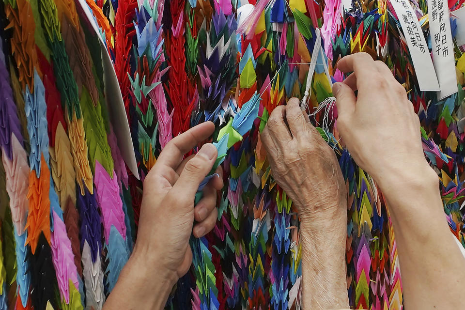 Hatsue Onda, center, is helped by Kengo Onda to offer strings of colorful paper cranes to the victims of the 1945 Atomic bombing near Hiroshima Peace Memorial Museum in Hiroshima, western Japan, Monday, Aug. 3, 2020. The origami cranes that can be seen throughout the city became a symbol of peace because of atomic bomb survivor Sadako Sasaki, who, while battling leukemia, folded similar cranes using medicine wrappers after hearing an old Japanese story that those who fold a thousand cranes are granted one wish. (AP Photo/Eugene Hoshiko)