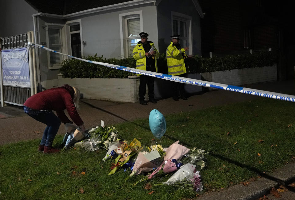 A woman places flowers amongst the floral tributes placed on one of the roads leading to the Belfairs Methodist Church in Eastwood Road North, where British Conservative lawmaker David Amess has died after being stabbed at a constituency surgery, in Leigh-on-Sea, Essex, England, Friday, Oct. 15, 2021. Police gave no immediate details on the motive for the killing of 69-year-old Conservative lawmaker Amess and did not identify the suspect, who was being held on suspicion of murder. (AP Photo/Kirsty Wigglesworth)