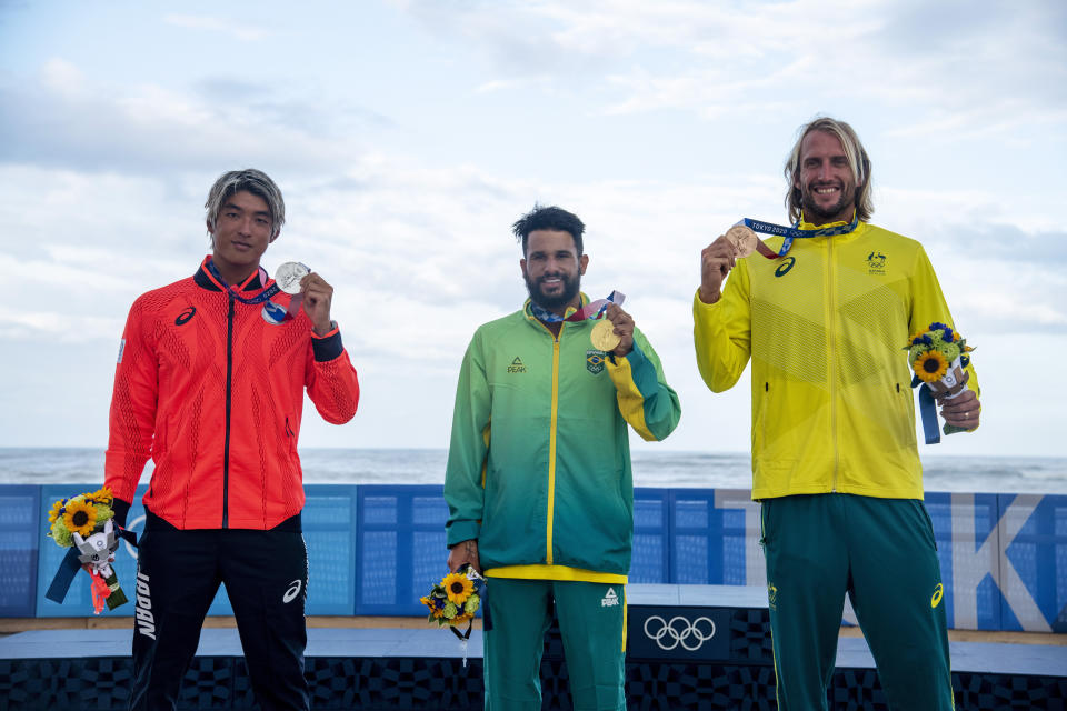 Brazil's Italo Ferreira, center, holding the gold medal, Japan's Kanoa Igarashi, left, silver medal, and Australia's Owen Wright, bronze medal, pose for photographers in the men's surfing competition at the 2020 Summer Olympics, Tuesday, July 27, 2021, at Tsurigasaki beach in Ichinomiya, Japan. (Olivier Morin/Pool Photo via AP)