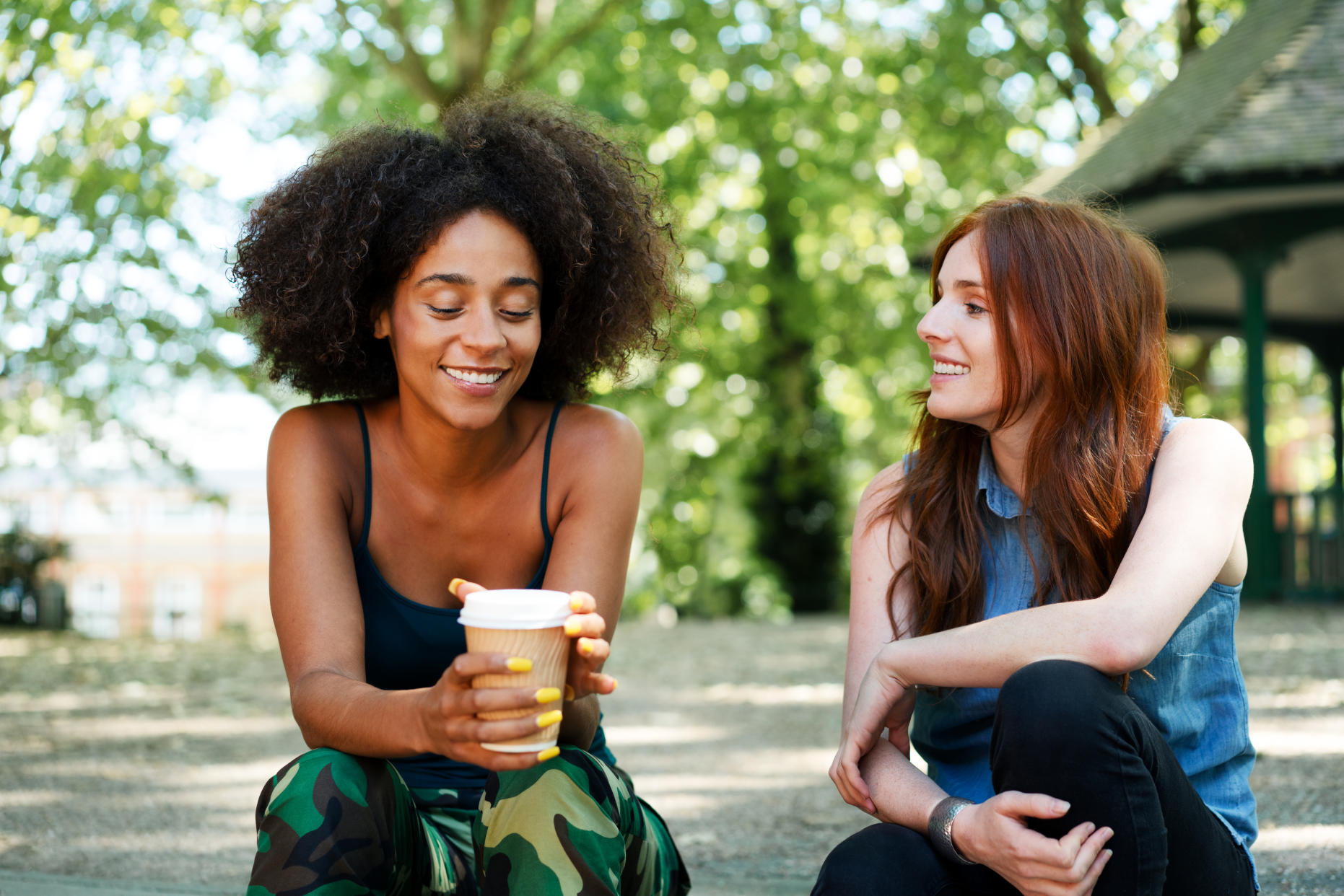 Two friends sat outside chatting, both smiling, one with a take away drink