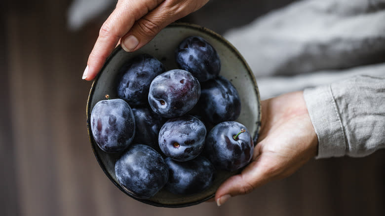 person holding bowl of black plums