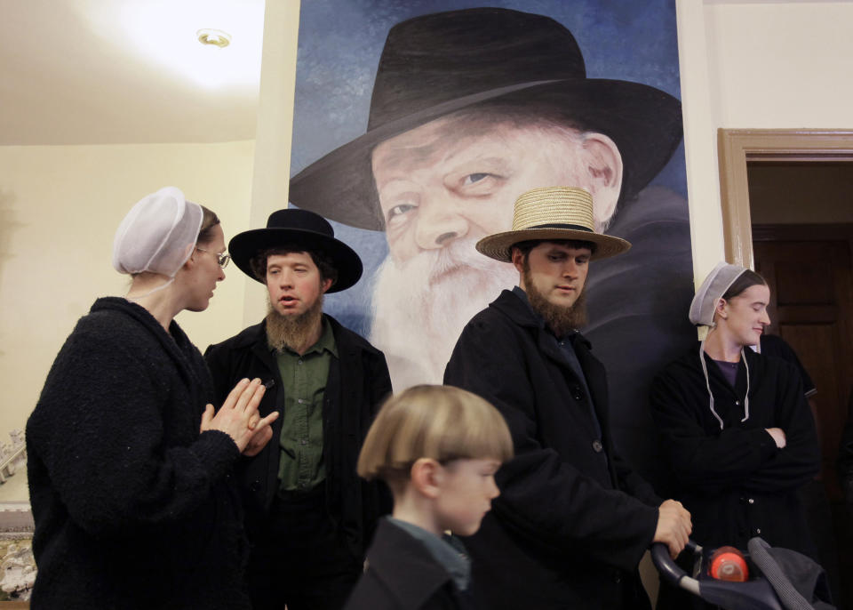 FILE - Anna Stoltzfus, left, talks with her husband Matthew Stolzfus in front of a portrait of the late Lubavitcher Rabbi Menachem Schneerson, while taking a tour with John Lapp, center, his son Jonathon, 6, and wife Priscilla, at a museum Tuesday, March 31, 2009 in the Crown Heights neighborhood of Brooklyn, New York. The city's ultra-Orthodox Jews took a group of Pennsylvania Amish on a walking tour of their world Tuesday, saying their communities are naturally drawn to each other with a commitment to simpler lifestyles. (AP Photo/Julie Jacobson, File)