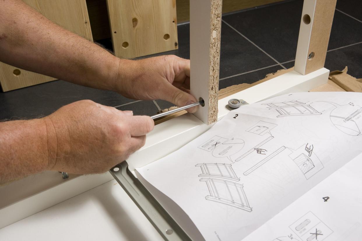 A man follows instructions to build an IKEA flat-pack chest of drawers at home.