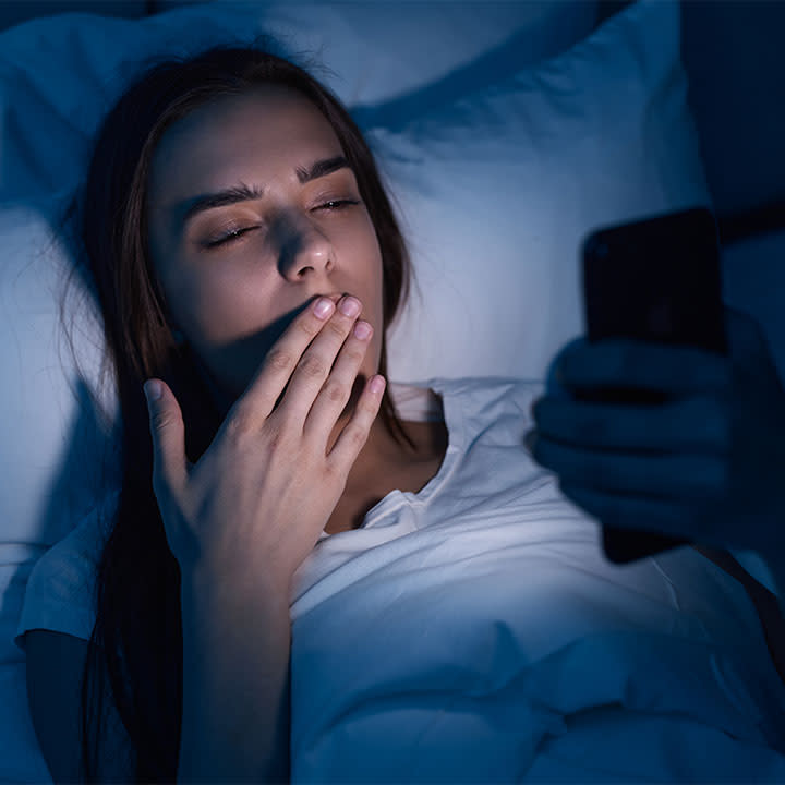 girl holding phone in bed and yawning