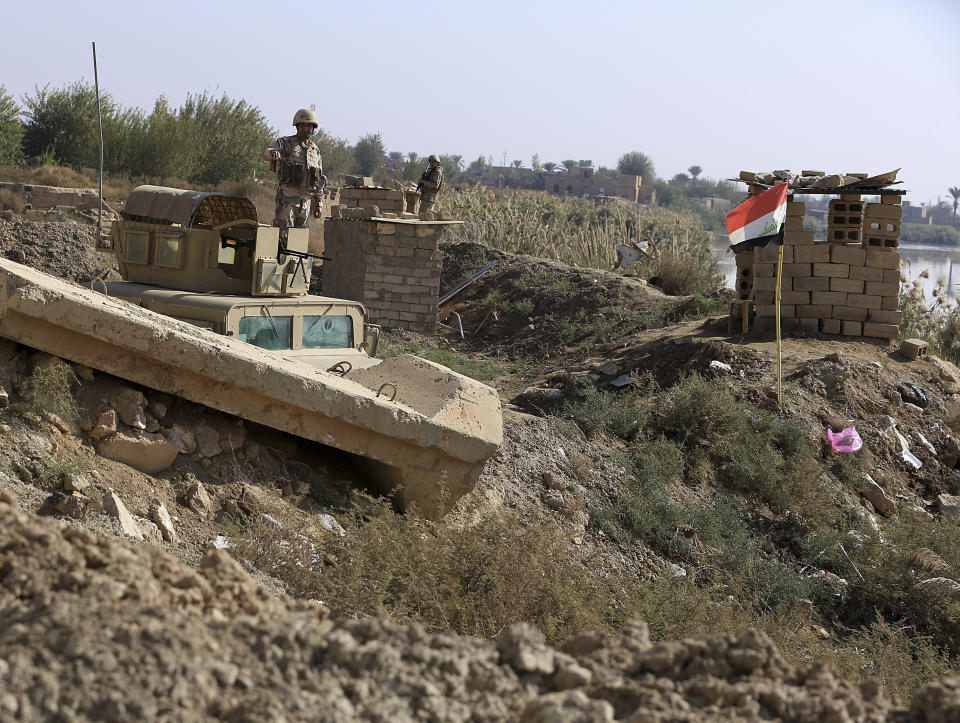 In this Tuesday, Nov. 13 2018 photo, Iraqi soldiers stand on the Iraqi side of the border with Syria, in the town of Qaim, Anbar province, Iraq. Life in Qaim has been put on hold as just across the border in Syria, fighting rages against one of the last major enclaves of the Islamic State group. (AP Photo/Hadi Mizban)