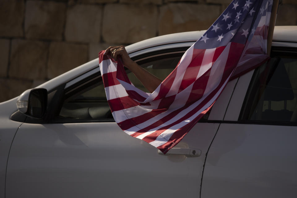 An Israeli supporter of U.S. President Donald Trump for re-election waves an American flag from her car as she headed for a rally outside of the U.S. Embassy, in Jerusalem, Tuesday, Oct. 27, 2020. (AP Photo/Maya Alleruzzo)