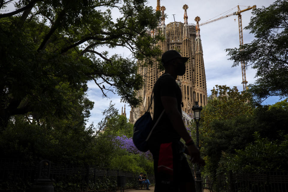 In this Sunday, May 31, 2020 photo, local visitors walk in a park next to the Antoni Gaudí's La Sagrada Familia Basilica in Barcelona. Tourism is a pillar of Spain's economy. Eighty million annual visitors generate 12% of Spain's GDP and help employ 2.6 million people. (AP Photo/Emilio Morenatti)