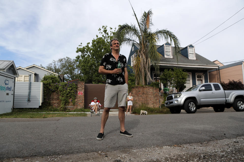 Marco St. John exercises social distancing as he listens to a front porch concert by his wife, singer Anais St. John, and pianist Harry Mayronne in New Orleans, Saturday, April 11, 2020. With New Orleans music venues shuttered for more than a month now because of the coronavirus outbreak, musicians and fans are finding new places to connect – porches, living rooms, studios and lawns – and reaching their largest audiences online, many streaming performances live on social media platforms. But for the city's club owners awaiting the green light to reopen there's concern about all the uncertainties, like how long it may take tourists to return, how soon the music scene will rebound and when it does, what it will look like. (AP Photo/Gerald Herbert)