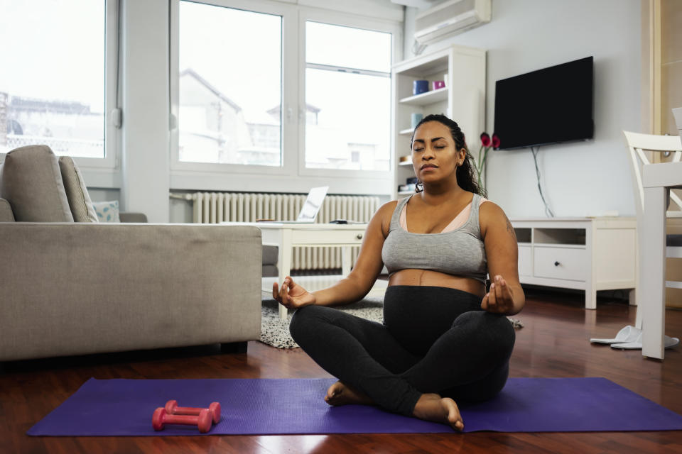 A woman sitting cross-legged on a yoga mat in her living room, practicing mindfulness