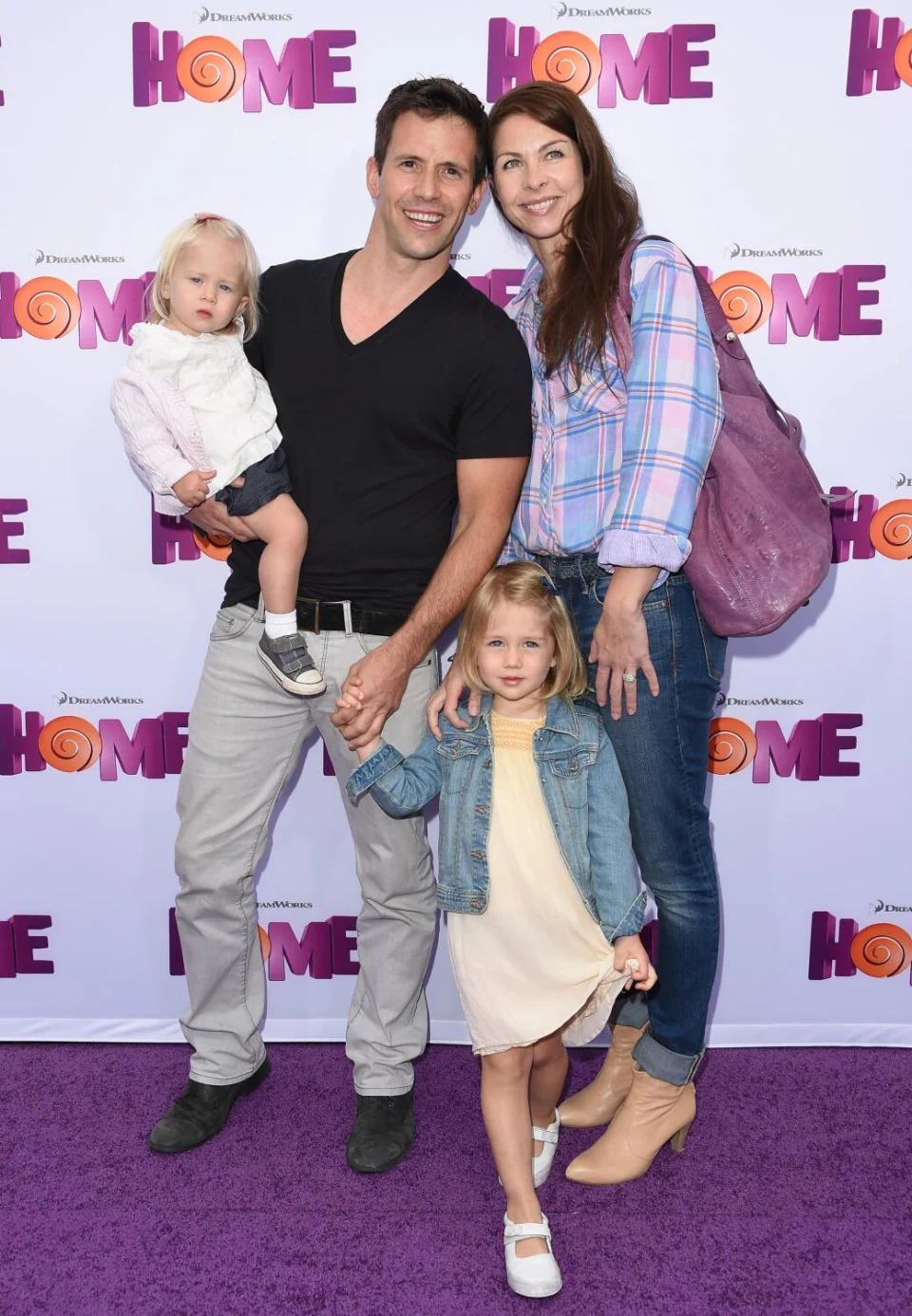 A man and a woman in casual wear holding two young girls posing for pictures on a purple carpet