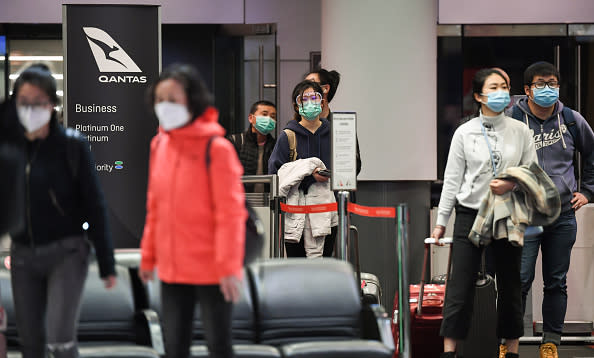 Passengers wearing face masks wait to be interviewed and temperature checked by New South Wales health officials after they arrive from a Qantas flight that flew from Melbourne at Sydney Airport in Sydney, Australia. 