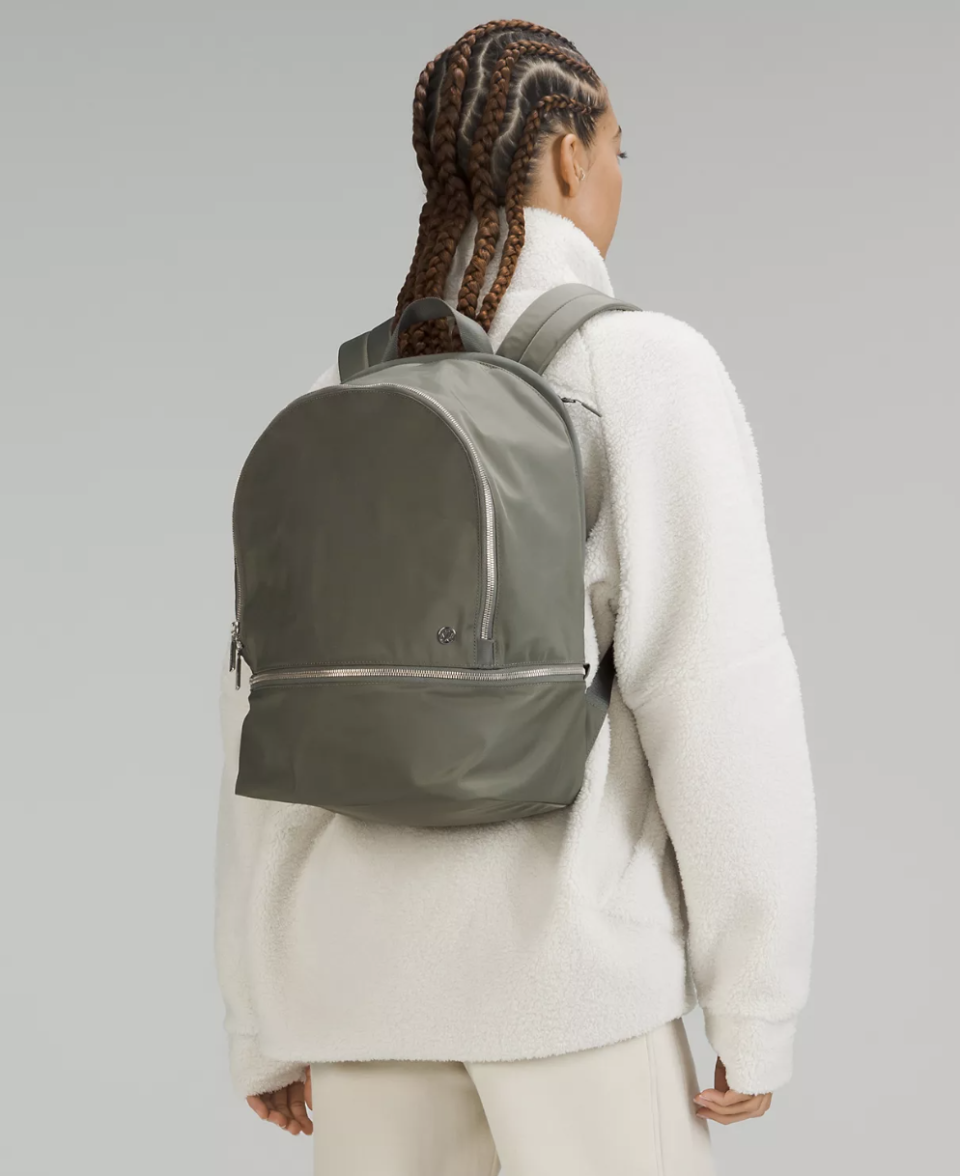 woman wearing white sweater, white pants and green City Adventurer Backpack 20L (photo via Lululemon)