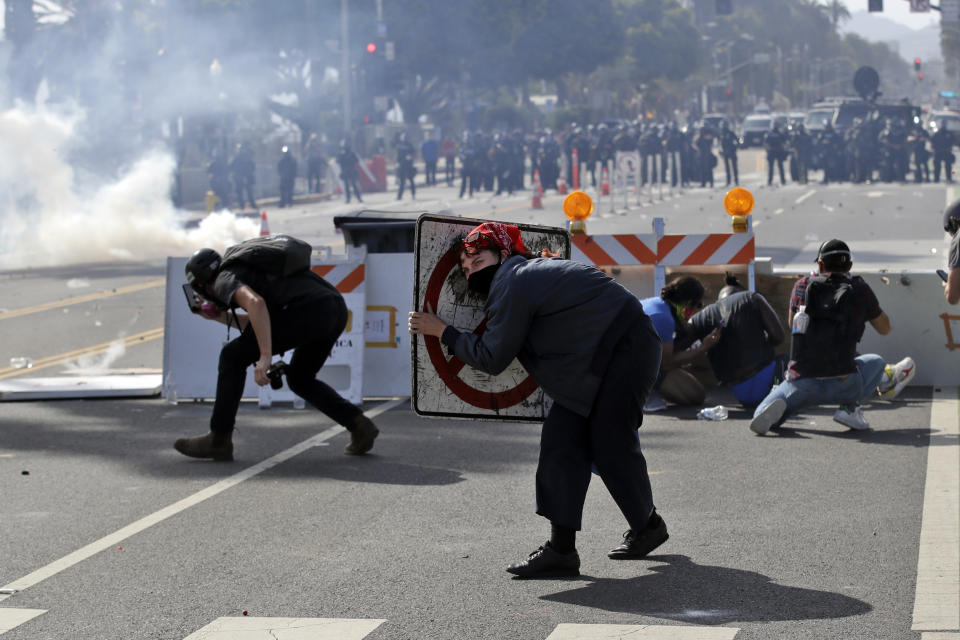 A demonstrator tries to shield herself from tear gas with a street sign during clashes with police Sunday, May 31, 2020, in Santa Monica, Calif. during unrest and protests over the death of George Floyd, a black man who was in police custody in Minneapolis. Floyd died after being restrained by Minneapolis police officers on May 25. (AP Photo/Marcio Jose Sanchez)