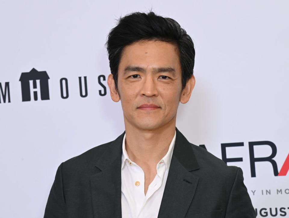 John Cho posing in a suit on a red carpet at an event