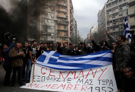 Greek farmers hold a Greek national flag and a banner reading "Germany pay us back now" during a protest against planned pension reforms outside the Agriculture ministry in Athens, February 12, 2016. REUTERS/Alkis Konstantinidis