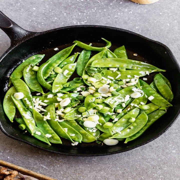 Snow peas in a skillet with scallions.