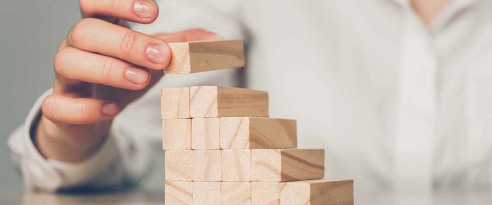 Business investment concept - hand builds a ladder from wooden blocks. Close up.