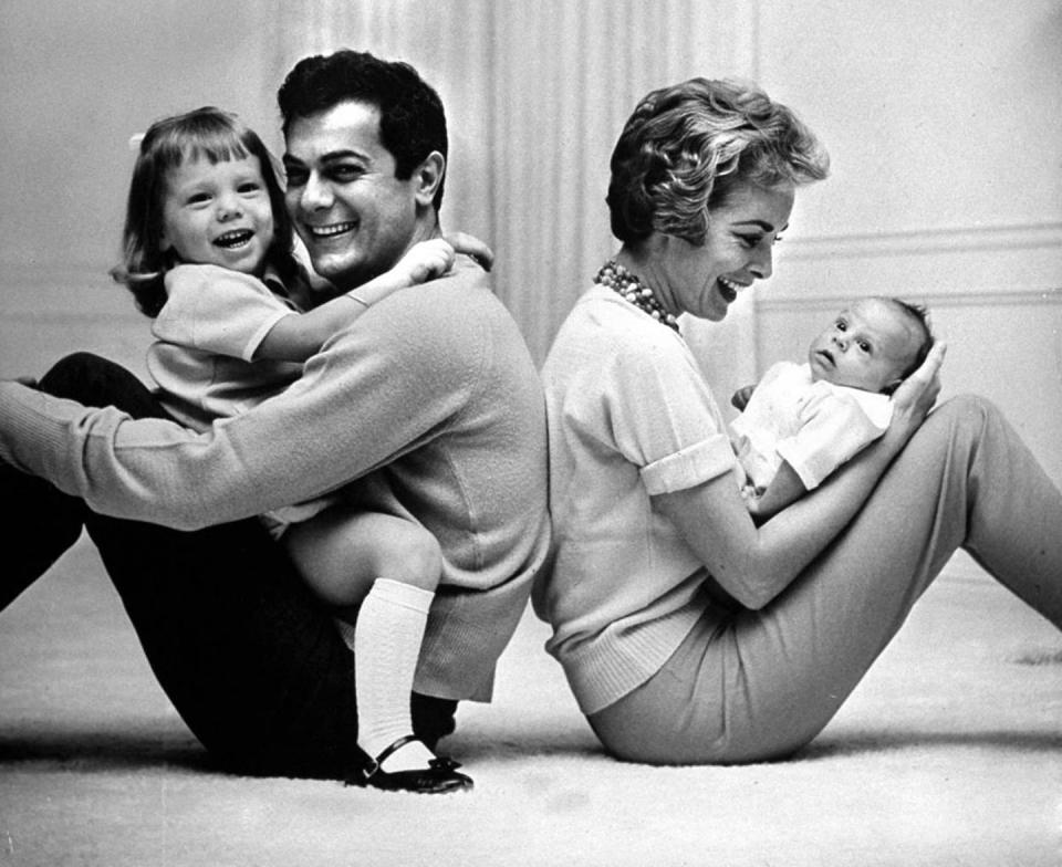 a black and white photo of tony curtis and janet lehigh sitting on the floor, laughing, with each holding a small child