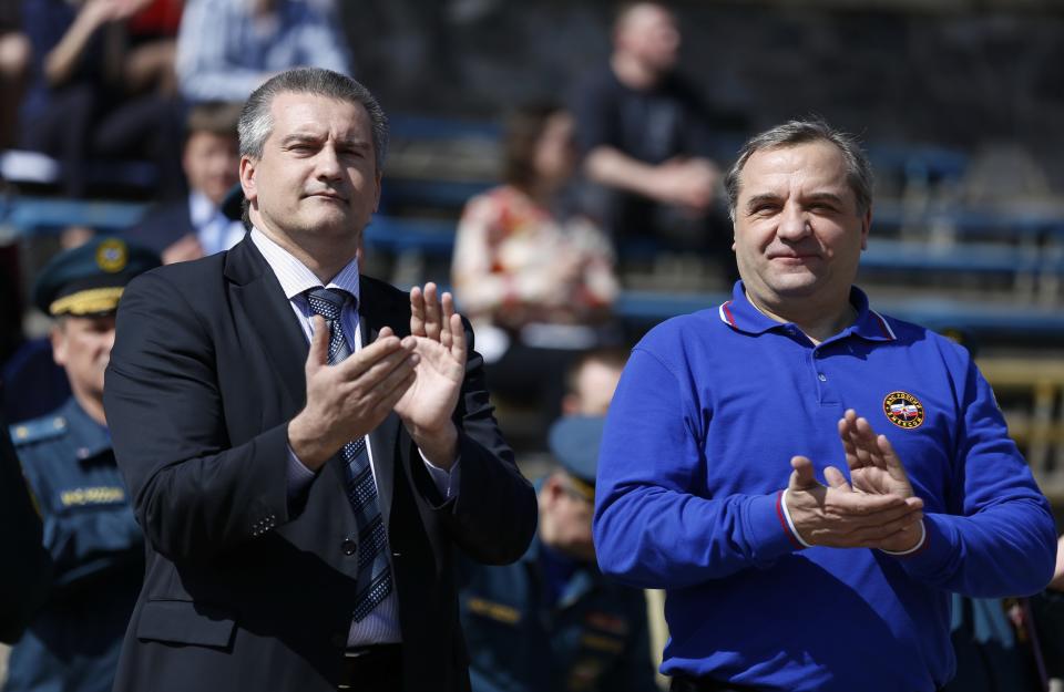 Crimean Premier Sergei Aksyonov, left, and Russian Emergency Situations Minister Vladimir Puchkov applaud at a meeting with emergency workers in Simferopol, Crimea, Tuesday, March 25, 2014. Puchkov met with local emergency officials in Simferopol and said that Russia sent diesel generators to Crimea to serve as a back-up in case of power outages. Crimea faced power cutoffs after Ukraine briefly cut energy supplies to the region. (AP Photo/Maxim Vetrov)