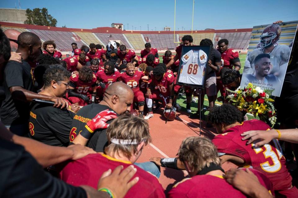 The parents of Sacramento City College football player Justin McAllister, Mary and Lloyd McAllister, at left, are surrounded in a huddle with team members during a ceremony to honor him prior to their game at Hughes Stadium on Saturday, Sept. 16, 2023. Justin died during a practice on Sept. 11.