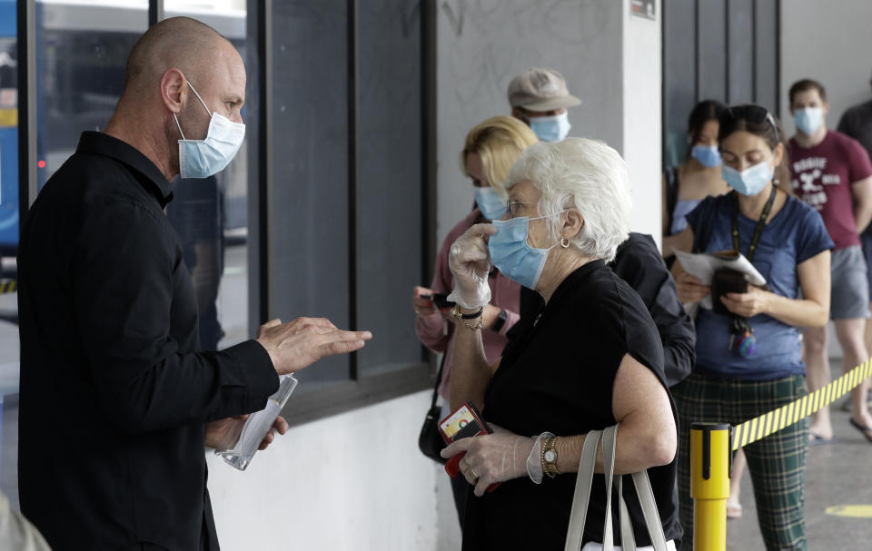 A staff member questions people as they wait in a line at a COVID-19 testing station on the northern beaches in Sydney, Australia, Monday, Dec. 21, 2020. Sydney's northern beaches are in a lockdown similar to the one imposed during the start of the COVID-19 pandemic in March as a cluster of cases in the area increased to more than 80. (AP Photo/Mark Baker)