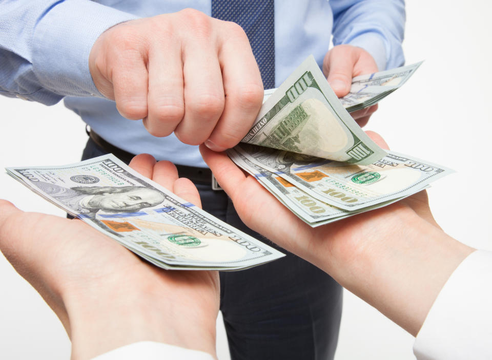 A businessmen in a tie placing crisp hundred dollar bills into two outstretched hands.