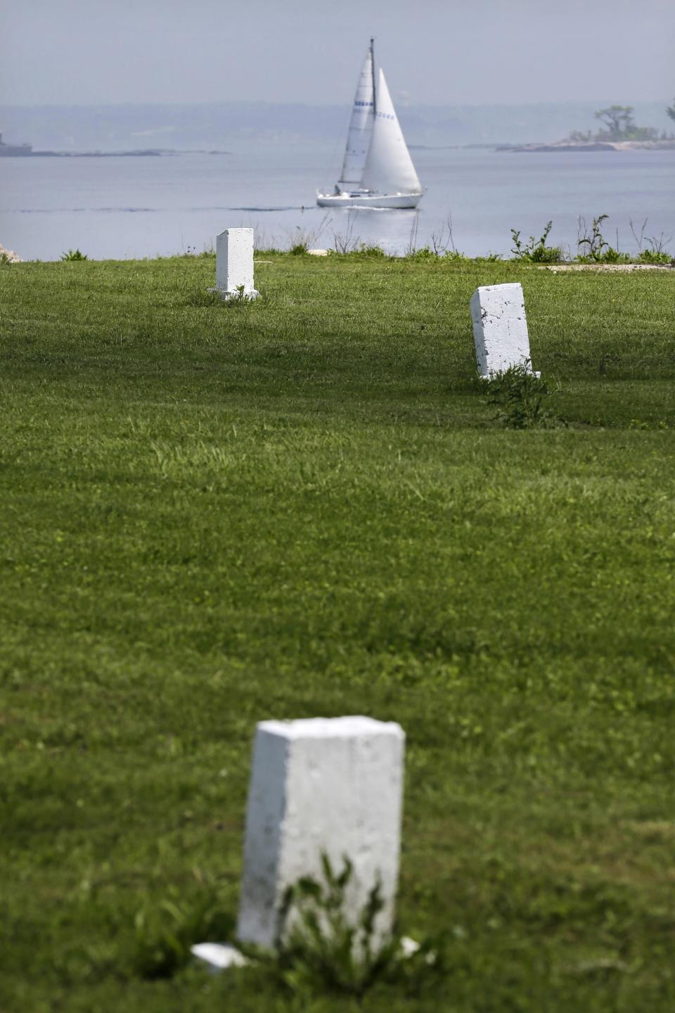 FILE - In this May 23, 2018, file photo, a sailboat passes by Hart Island where white markers indicate a mass grave of about 150 people in New York. The island has served as New York City's potter's field for 150 years, where part of the graveyard along the island's shoreline is gradually washing away. (AP Photo/Seth Wenig, File)