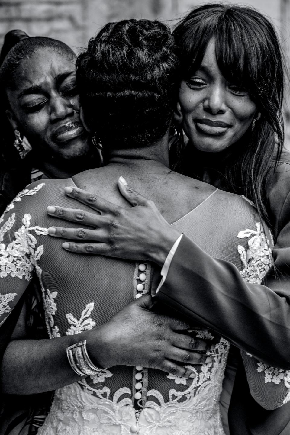 Two women cry as they hug a bride.