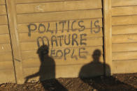 People stand near a wall with a poltical graffiti message in this Monday, Aug, 17, 2020 photo. Unable to protest on the streets, some in Zimbabwe are calling themselves "keyboard warriors" as they take to graffiti and social media to pressure a government that promised reform but is now accused of gross human rights abuses.(AP Photo/Tsvangirayi Mukwazhi)