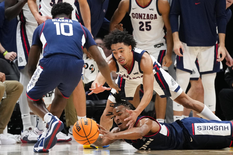 UConn guard Stephon Castle reaches out for the ball as he falls to the court, as guard Hassan Diarra (10) and Gonzaga guard Ryan Nembhard watch during the second half of an NCAA college basketball game Friday, Dec. 15, 2023, in Seattle. (AP Photo/Lindsey Wasson)