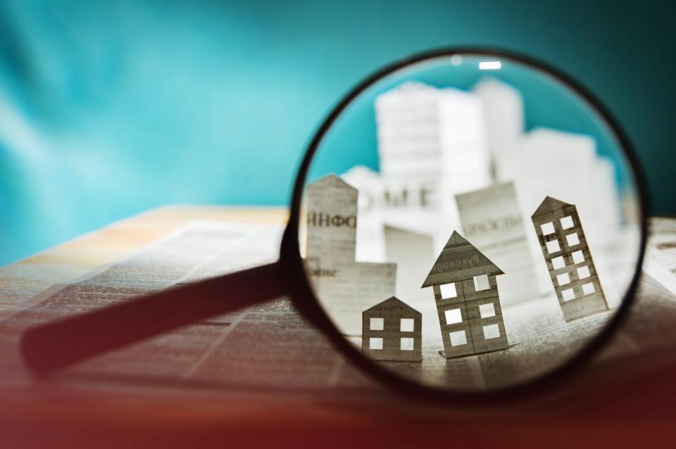 A magnifying glass focuses on newspaper cutouts of real estate properties.