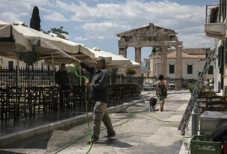 Un hombre limpia las sombrillas de su restaurante en el distrito de Plaka, Grecia