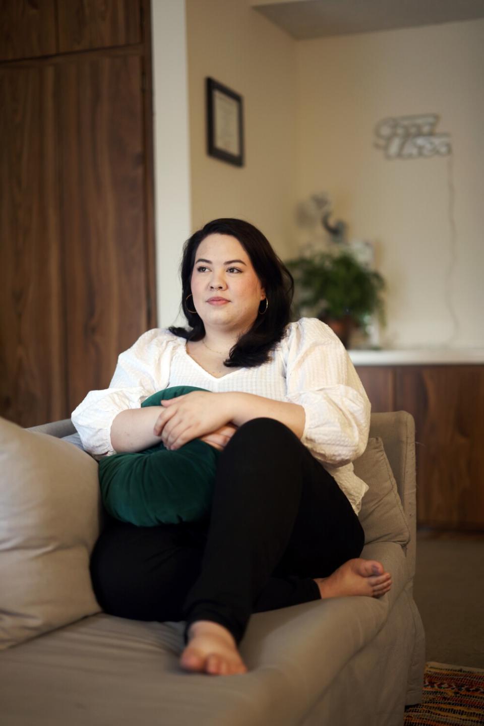 Kayla Camacho sitting cross-legged on a couch holding a pillow