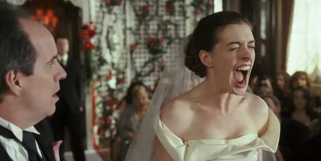 Anne Hathaway in a wedding dress screams with her mouth wide open during a wedding ceremony. A man next to her looks on