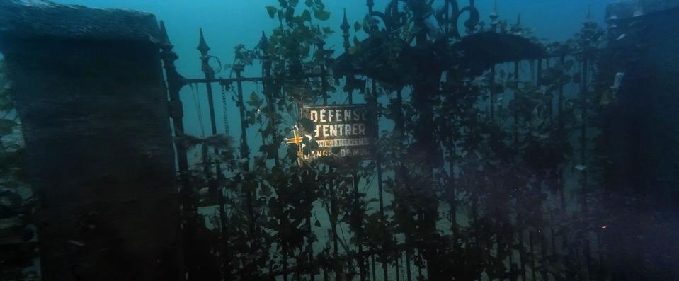 A diving cameraman comes across a gate toward an underwater house in "The Deep House"