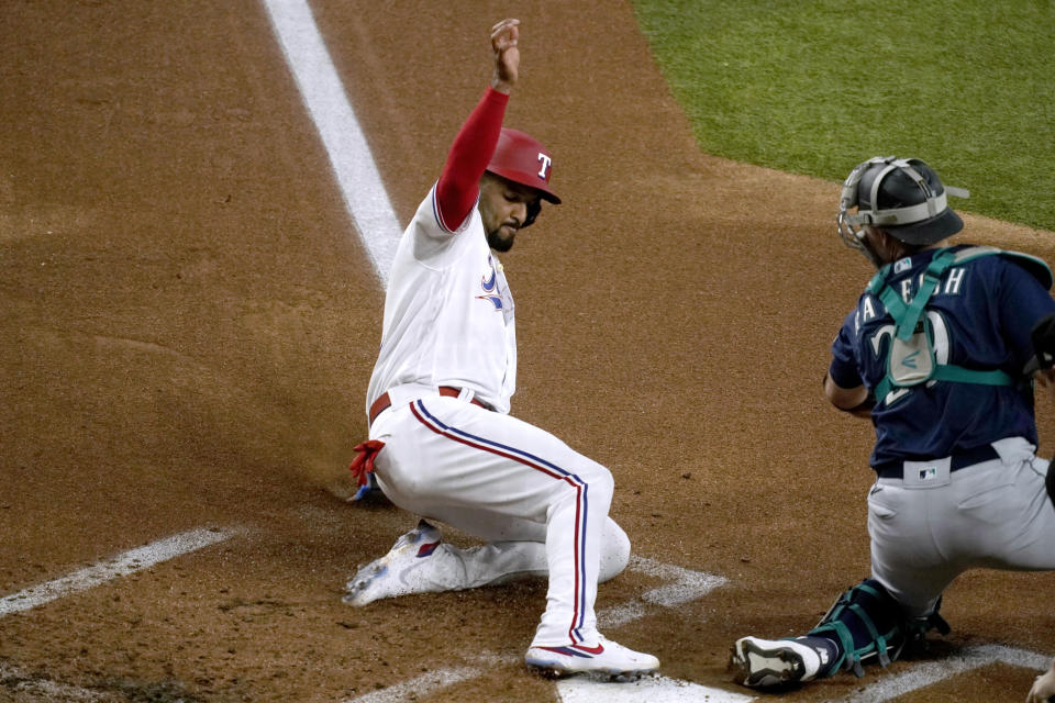 Texas Rangers' Marcus Semien scores a Corey Seager double, next to Seattle Mariners catcher Cal Raleigh during the first inning of a baseball game Thursday, July 14, 2022, in Arlington, Texas. (AP Photo/Tony Gutierrez)