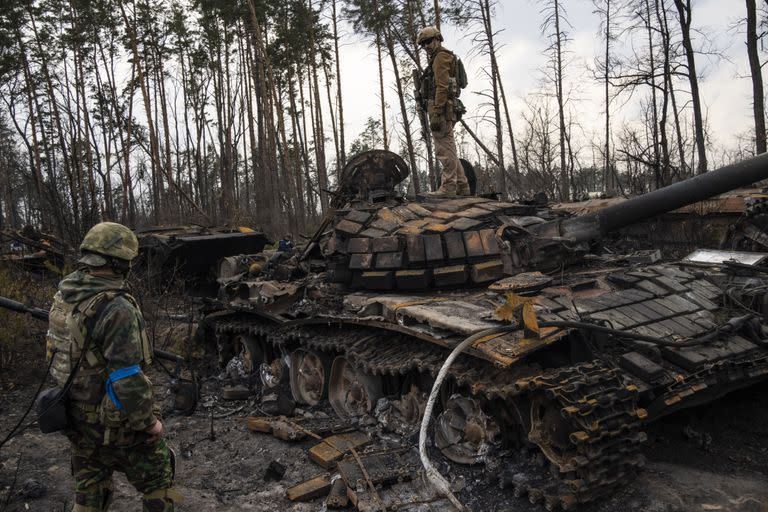 Un soldado ucraniano permanece encima de un tanque ruso destruido mientras otro lo mira, en las afueras de Kiev, Ucrania. (AP Foto/Rodrigo Abd)