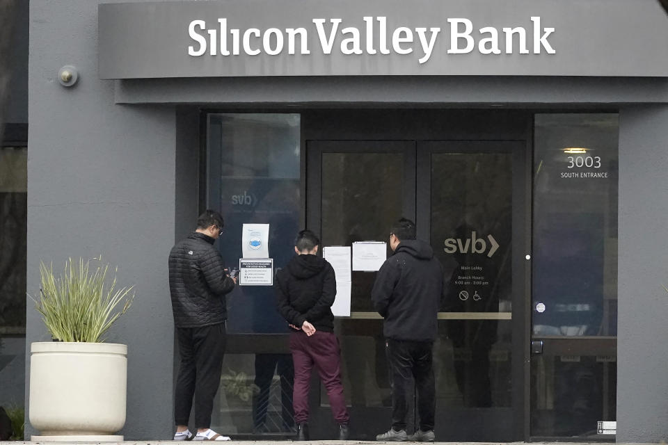 People look at signs posted outside of an entrance to Silicon Valley Bank in Santa Clara, Calif., Friday, March 10, 2023. From winemakers in California to startups across the Atlantic Ocean, companies are scrambling to figure out how to manage their finances after their bank, Silicon Valley Bank, suddenly shut down on Friday. The meltdown means distress not only for businesses but also for all their workers whose paychecks may get tied up in the chaos. (AP Photo/Jeff Chiu)