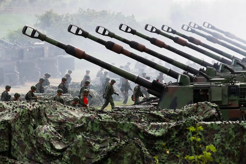 A row of American self-propelled howitzers is pictured, with Taiwanese soldiers walking towards them in the background.