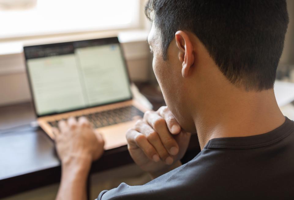 A person works on a laptop, focused on the screen. The workspace is minimal with a glimpse of a window in the background