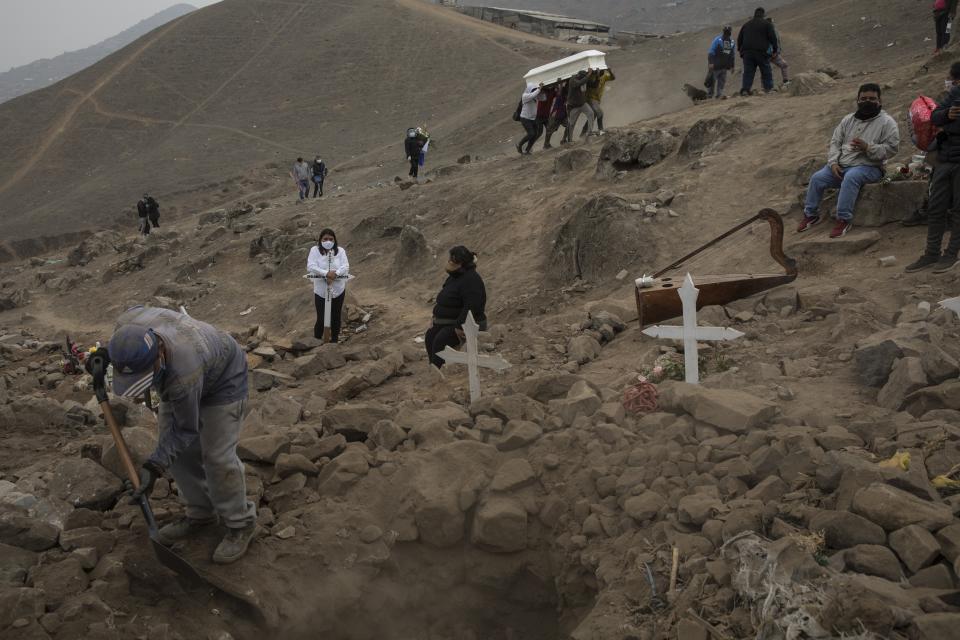 A cemetery worker shovels dirt into a grave that contains the remains of Apolonia Uanampa who died from the new coronavirus, as the coffin that contains the remains of Demetria Huamani, also a victim of the virus, is carried to her burial site at the Nueva Esperanza cemetery on the outskirts of Lima, Peru, Wednesday, May 27, 2020. The virus initially brought to the region largely by wealthy citizens or visitors coming from Europe and the United States is now increasingly concentrated in poorer neighborhoods where residents have few means of protecting themselves. (AP Photo/Rodrigo Abd)